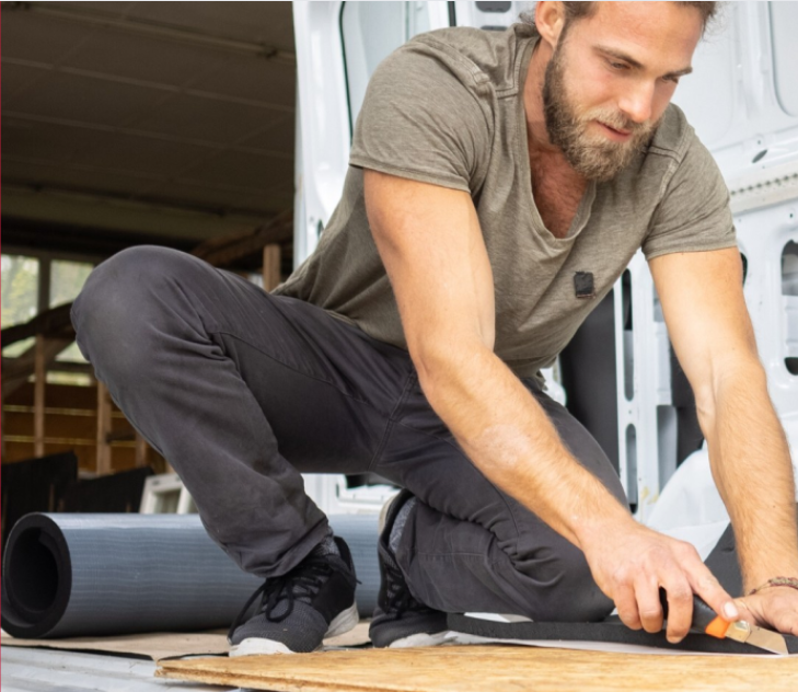 Man cutting Armaflex insulation sheet inside a campervan during a van conversion