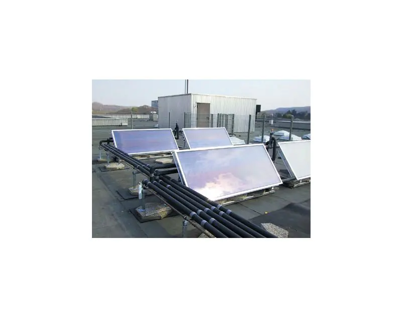 A rooftop installation of solar panels connected by black Armaflex HT Solar Pipe Insulation, running along the base of the panels. The setup is on a flat roof with a small building and a distant landscape in the background, showcasing the insulation’s use